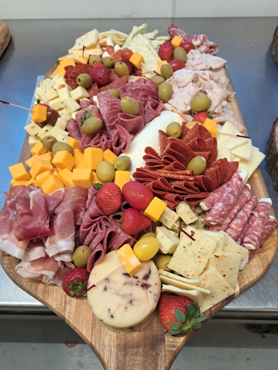 A full charcuterie board with sliced meats, cheeses, olives, strawberries, and turkey