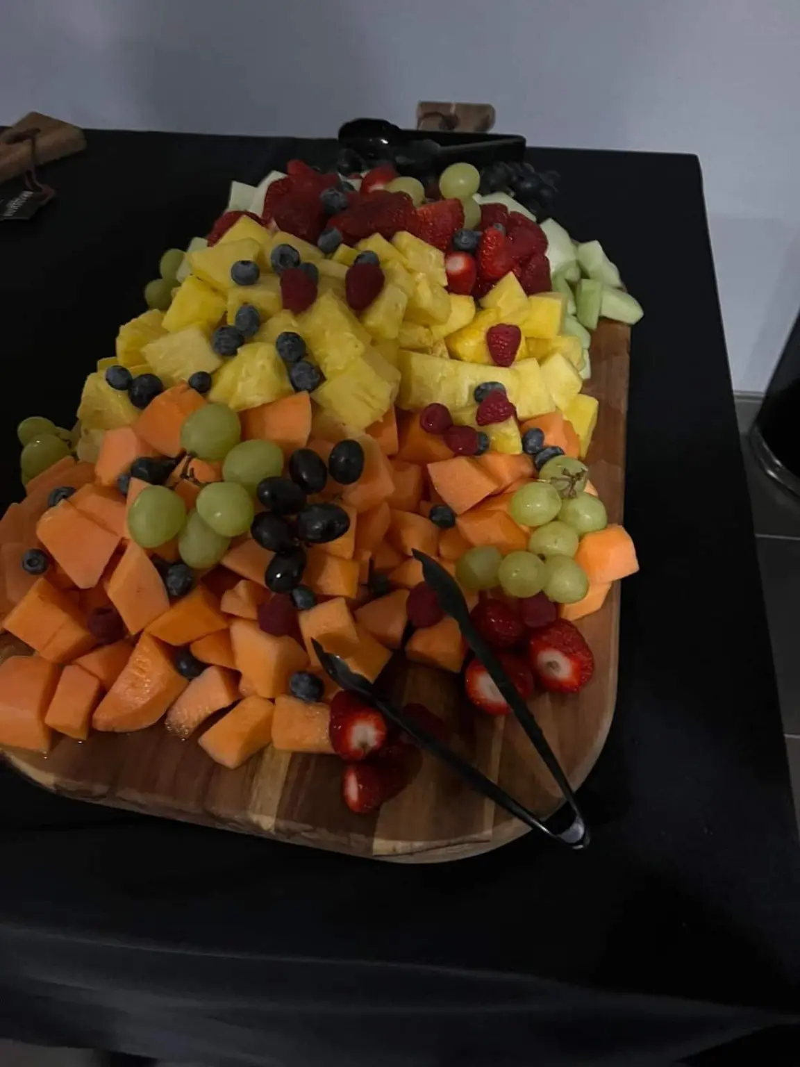 A fresh fruit board arranged with pineapple, melon, berries, and grapes